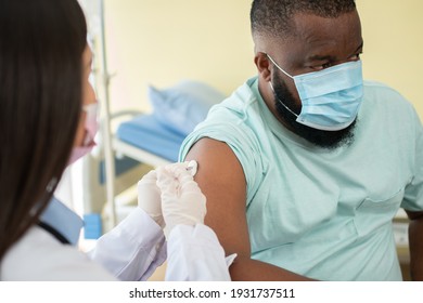 Asian doctor user syringe needle for injection vaccinate,  African American is being covid vaccinated for prevention coronavirus and flu. Concept of immunization from inoculation
