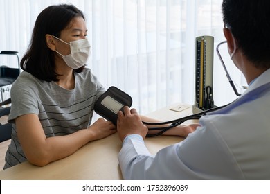 Asian Doctor Using Sphygmomanometer To Measure Blood Pressure Of The Woman Patient That Has Hypertension And Visit Him At Outpatient Clinic Of Hospital. Healthcare And Medical Concept