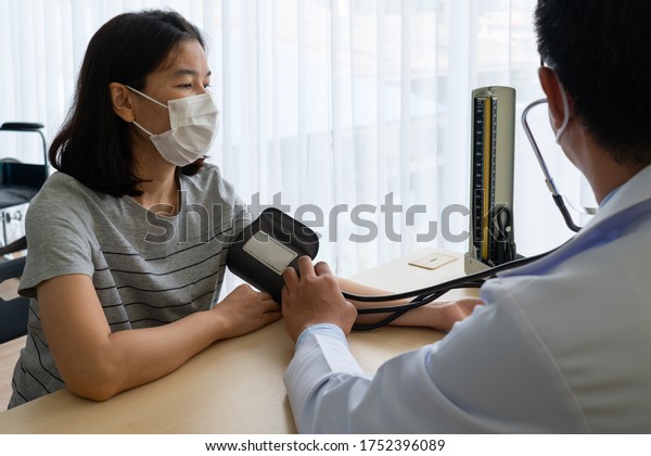 Asian\
doctor using sphygmomanometer to measure blood pressure of the\
woman patient that has hypertension and visit him at outpatient\
clinic of hospital. healthcare and medical\
concept