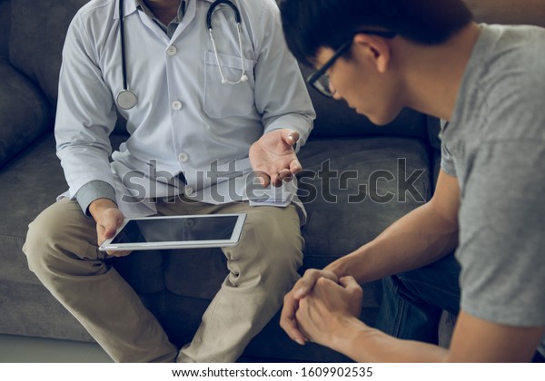 Asian doctor visited the patient at home while\
using the tablet explaining the patient condition and the treatment\
result.