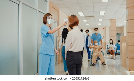 Asian doctor walk through hospital hallway with helper staff push patient wheelchair, operator check fever by digital thermometer visitor at information counter for scan and protect from coronavirus. - Powered by Shutterstock