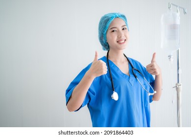 Asian Doctor Wearing A Blue Surgical Gown Thumbs Up There Is A Bag Of Saline On The Side.