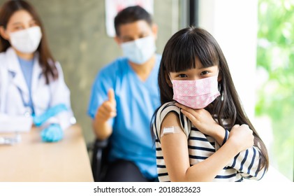 Asian  Doctor Wearing Gloves And Isolation Mask Is Making A COVID-19 Vaccination In The Shoulder Of Child Patient With Her Mother At Hospital.