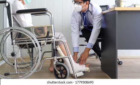 asian doctor wearing mask examines the woman patient who sits in wheelchair because she gets leg injury. healthcare and medical concept