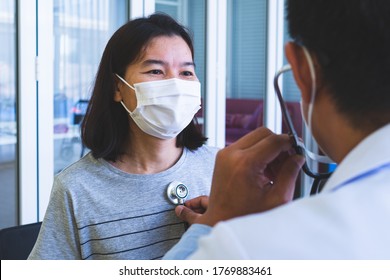 Asian Doctor Wearing Mask Using Stethoscope To Listening Heart Of   Woman Patient Who Come To Visit At Hospital For Sickness. Healthcare And Medical Concept