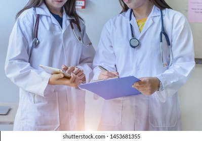 Asian Doctors Holding Clipboard ,iPad Talking And Discussion About Patient At Hospital