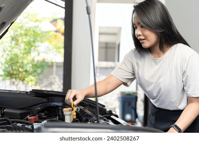 Asian driver woman checking car radiator problems, female checks break down vehicle engine. Woman checking oil level in car engine at home. Concept of car maintenance and garage. - Powered by Shutterstock