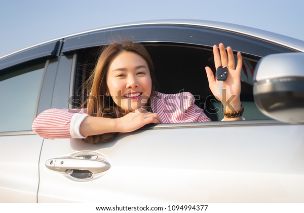 Asian driver woman smiling and showing new car key\
while sitting in a car that she taking it from dealer in the auto\
show. transport business, sale for consumerism and people\
concept,vintage color
