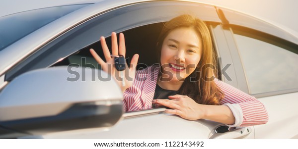Asian driver woman smiling and showing new car key\
while sitting in a car that she taking it from dealer in the auto\
show. transport business, car sale for consumerism and people\
concept,vintage color