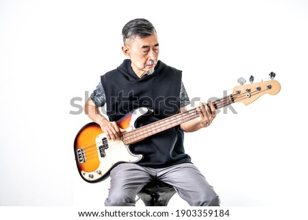 An Asian elder cool man has fashion in gray t-shirt And black vest learn to play bass guitar. Shoot On white background in the studio. Positive active old cool senior healthy retirement concept.