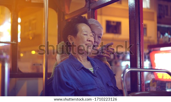 Asian elder couple have fun travel through Hong\
Kong city tram at night