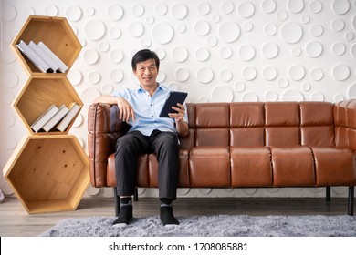 Asian Elder Man Age Between 50-60 Years Old Focus On Reading On Tablet In Living Room With Copy Space. Retired Man Relaxing At Home And Spending A Time In Learning, Wellness And Spiritual Meditation.