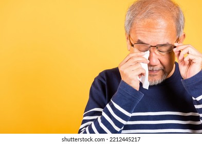 Asian Elder Man Crying Raise Glasses With Tissue Wipe Red Eyes Studio Shot Isolated On Yellow Background, Portrait Senior Old Man Sad Wiping Away His Tears, Upset Depressed Lonely