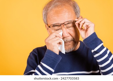 Asian elder man crying raise glasses with tissue wipe red eyes studio shot isolated on yellow background, Portrait senior old man sad wiping away his tears, Upset depressed lonely - Powered by Shutterstock