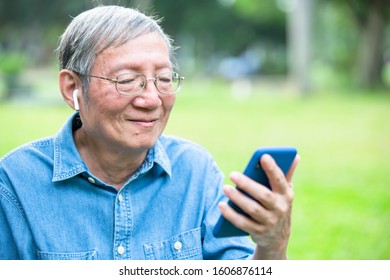 Asian Elder Man Use Ear Buds With Smart Phone In The Park