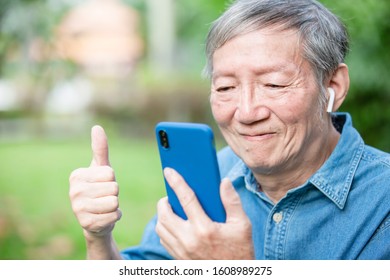 Asian Elder Man Use Ear Buds With Smart Phone And Has Thumb Up Gesture In The Park