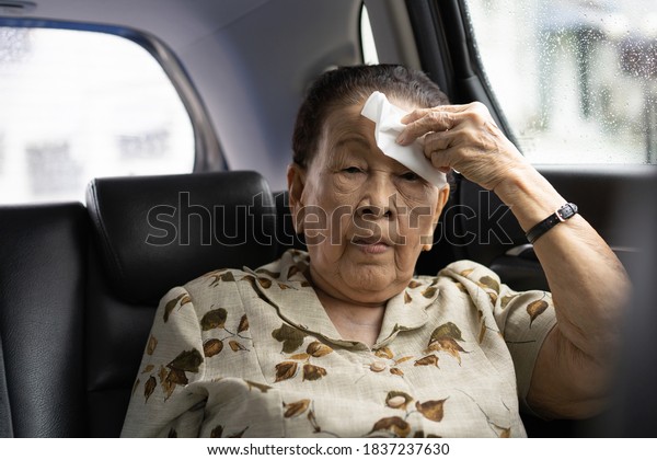 Asian elder woman age between 80 - 90 years old\
using a hygiene tissues to clean up her mouth and facial while\
traveling by the taxi. Hygienic lifestyle and healthcare in old\
people concept.