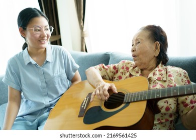 Asian elder woman playing an acoustic guitar and let her granddaughter taking a video on smartphone close up with copyspace. Elder Asian woman making a online video live streaming on social network.