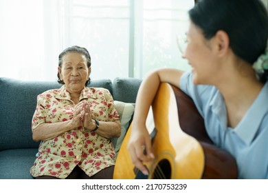 Asian elder woman playing an acoustic guitar and let her granddaughter taking a video on smartphone close up with copyspace. Elder Asian woman making a online video live streaming on social network.
