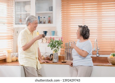 Asian Elderly Couple Drinking Warm Coffee And Talking Together In Kitchen At Home. Chinese Couple Enjoy Love Moment While Taking Together At Home. Lifestyle Senior Family At Home Concept.