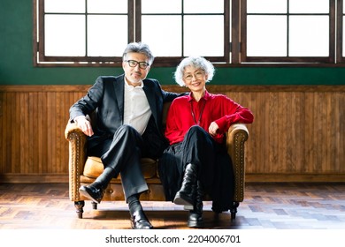 Asian Elderly Couple Sitting On Sofa In Fashionable Room.