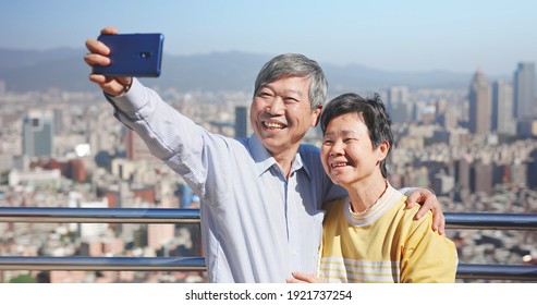 Asian Elderly Couple Take Selfie By Mobile Phone Together And Smile Happily Outdoor In City While Traveling