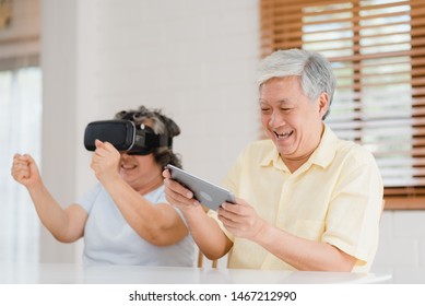 Asian elderly couple using tablet and virtual reality simulator playing games in living room, couple feeling happy using time together lying on table at home. Lifestyle Senior family at home concept. - Powered by Shutterstock