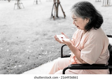 Asian Elderly Female Patient Sitting On A Wheelchair She Was Looking At The Blood On The Tissues, Which Used To Wipe The Mouth From Coughing, With Shock And Worry, To Emphysema And Health Concept.