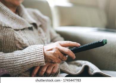 Asian Elderly Hand Holding Remote Television. Senior People Relax From Work Wear Sweater Sit On Sofa Watching Tv Movie In Living Room Stay At Home.