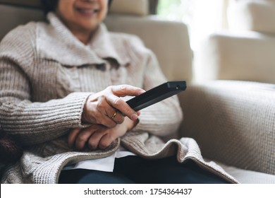 Asian Elderly Hand Holding Remote Television. Senior People Relax From Work Wear Sweater Sit On Sofa Watching Tv Movie In Living Room Stay At Home.