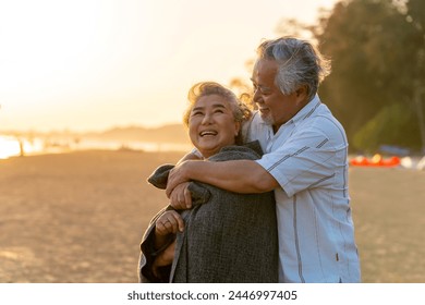 Asian elderly man covered his wife with a blanket and hugging each other on tropical beach at summer sunset. Retirement senior people family enjoy outdoor lifestyle travel ocean on summer vacation. - Powered by Shutterstock