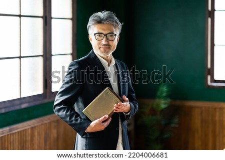 Asian elderly man holding a book in a stylish room