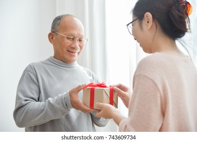 Asian elderly man receiving a brown gift box from young daughter for Christmas and New year. Happy Woman in glasses surprising to grandfather in Birthday. - Powered by Shutterstock