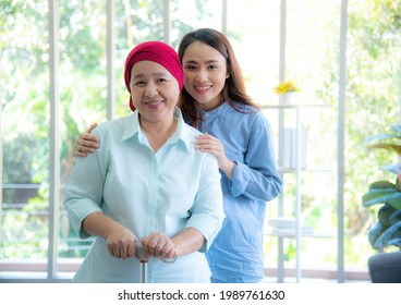 Asian elderly mother wearing red headscarf recover from cancer standing, holding walking stick and having her daughter by her side embrace, smile very happily. Cancer or leukemia survivor concept. - Shutterstock ID 1989761630