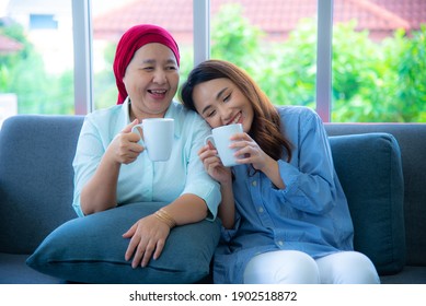 Asian elderly mother who recover from cancer and her daughter are sitting on a couch holding cup of drink and talking to one another very happily after chemotherapy. Cancer ,leukemia survivor concept. - Shutterstock ID 1902518872