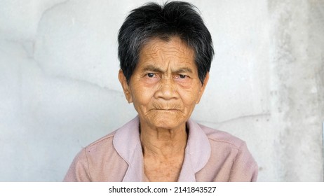 Asian Elderly Native Woman Looking To Camera With Serious Face, Smiling In Eyes Isolated Concrete Grey Wall Background. Concept Of People Rural Lifestyle, Expression.