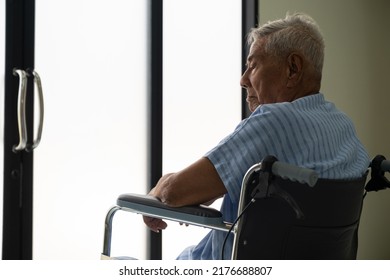 Asian Elderly Patient Male Sit On A Wheelchair Feel Alone , Sad And Looking Out The Door At The Hospital Ward. Lonely Old Male In Nursing Home. Loneliness Elder. Depressed Mature.
