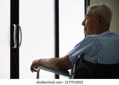 Asian Elderly Patient Male Sit On A Wheelchair Feel Alone , Sad And Looking Out The Door At The Hospital Ward. Lonely Old Male In Nursing Home. Loneliness Elder. Depressed Mature.
