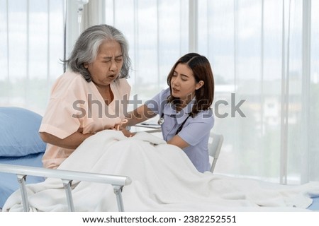 Asian elderly patient with stomachache. A nurse or caregiver for an elderly patient is helping a patient with severe stomach problems. Nurses care for patients in hospitals or clinics.