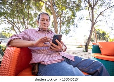 Asian Elderly People With Gray Hair Are Using Mobile Phones. A Happy Older Man Sitting On A Comfortable Sofa In The Garden.