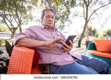 Asian Elderly People With Gray Hair Are Using Mobile Phones. A Happy Older Man Sitting On A Comfortable Sofa In The Garden.