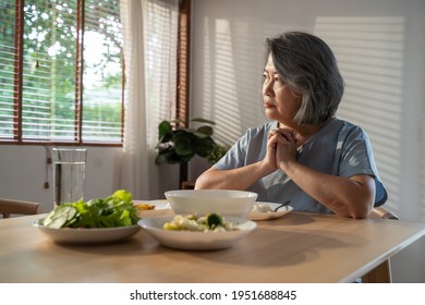 Asian Elderly Retired Grandmother Stay At Home With Painful Face Sitting Alone On Eating Table In House. Depressed Mature Senior Old Woman Upset Feeling Unhappy, Lonely And Missing Her Family At Home.