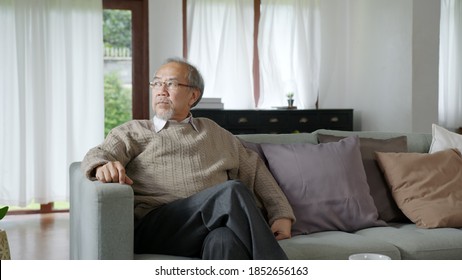 Asian Elderly Senior Male Or Depressed Grandpa At Nursing Home Living Room On Quarantine Looking Out Window Feeling Sad Missing Unhappy Thoughtful In Mental Health Care In Older People.