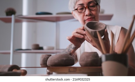 Asian elderly woman enjoying pottery work at home. A female ceramicist is making new pottery in a studio. - Powered by Shutterstock