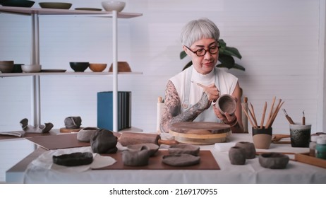 Asian elderly woman enjoying pottery work at home. A female ceramicist is making new pottery in a studio. - Powered by Shutterstock