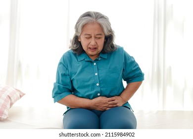 Asian elderly woman has a stomachache. She sat on the white bed. The concept of health care for the elderly. Illness. Health insurance. - Powered by Shutterstock