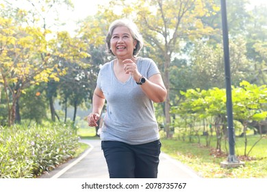 Asian Elderly Woman Jogging In The Park In The Morning She Smiles Happy Healthy Body. Concept Of Health Care For Seniors To Be Healthy