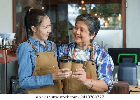 Asian elderly woman is retired. pensioner holds disposable coffee cup and clinks it with Asian daughter for promotional photo for coffee shop. The coffee shop is a family business with a happy smile.