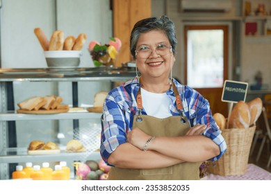 Asian elderly woman standing with arms crossed and smiling happily. After using pension after retirement Let's open small business coffee shop. in order to income in old age business can be forwarded