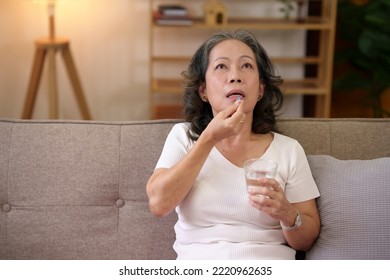 Asian Elderly Woman Taking Medicine In The Living Room At Home